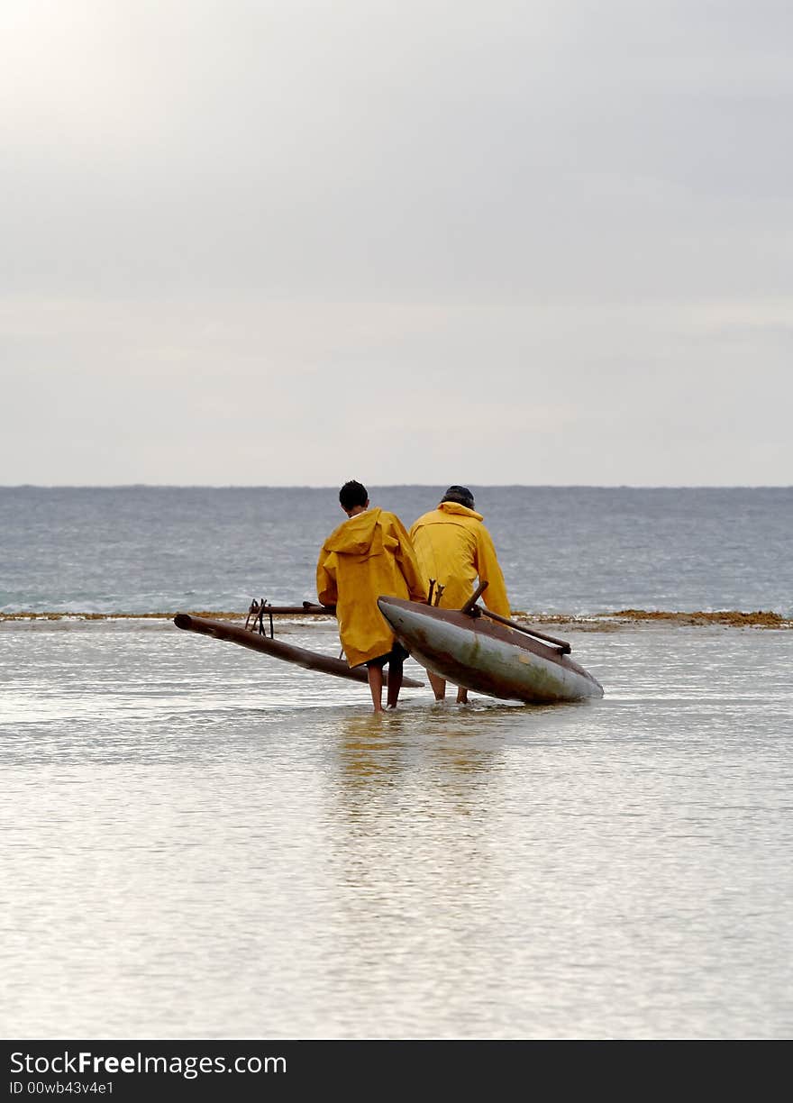 Fisherman and son carrying outrigger canoe across reef to launch it. Fisherman and son carrying outrigger canoe across reef to launch it