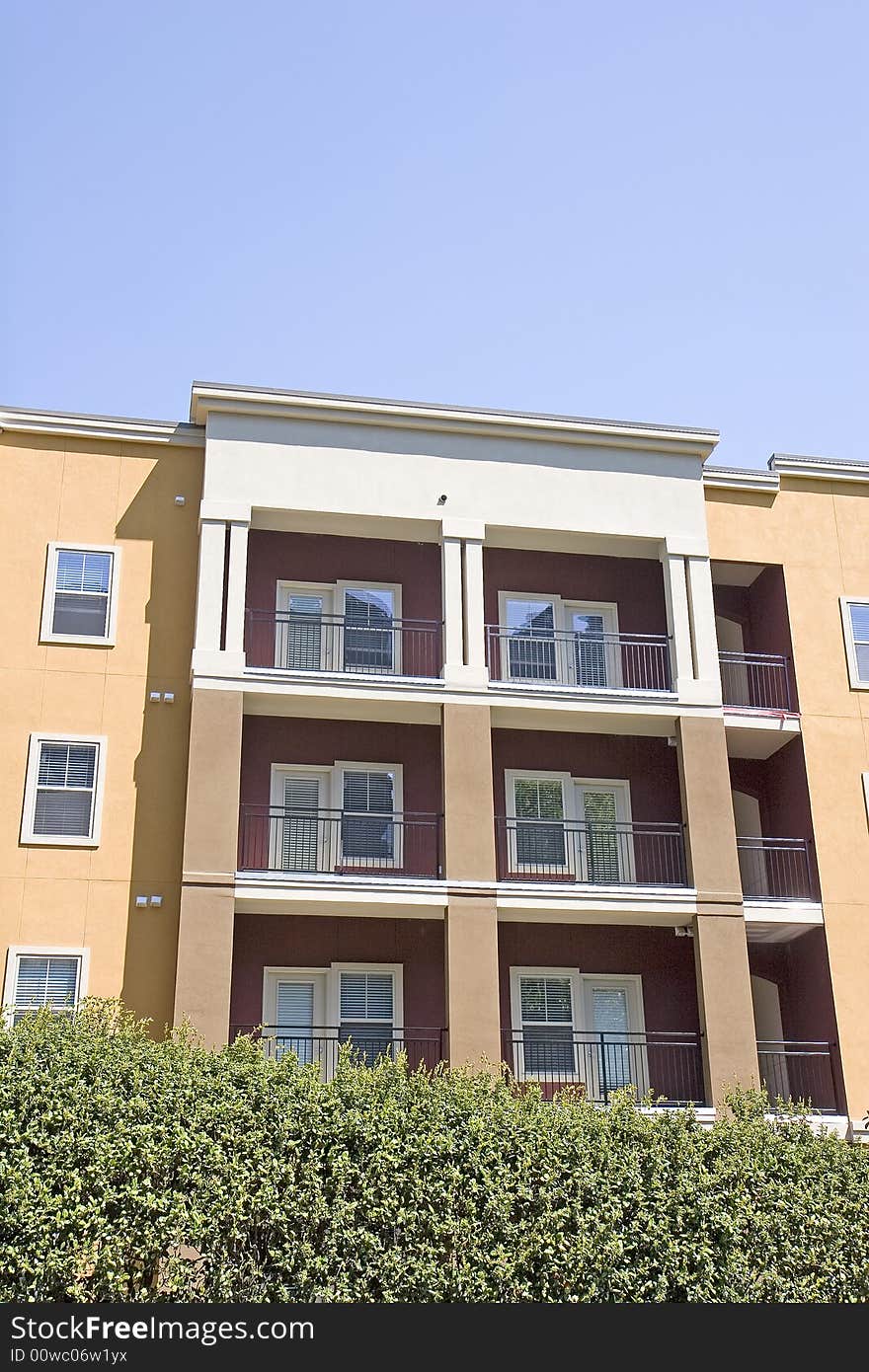 A colorful condo complex with balconies over a green hedge. A colorful condo complex with balconies over a green hedge