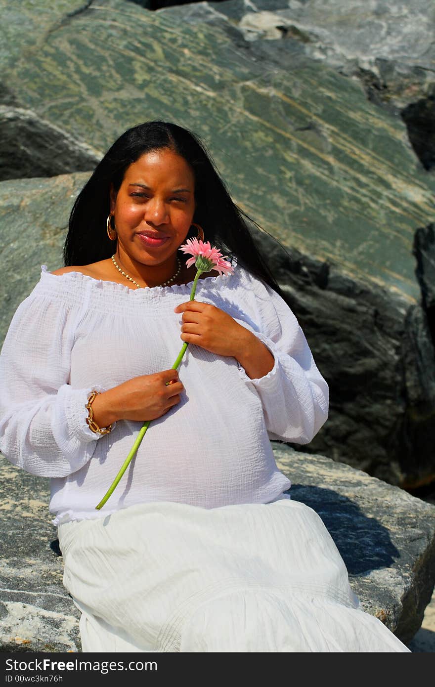 Woman sitting on the rocks and holding a pink flower. Woman sitting on the rocks and holding a pink flower.