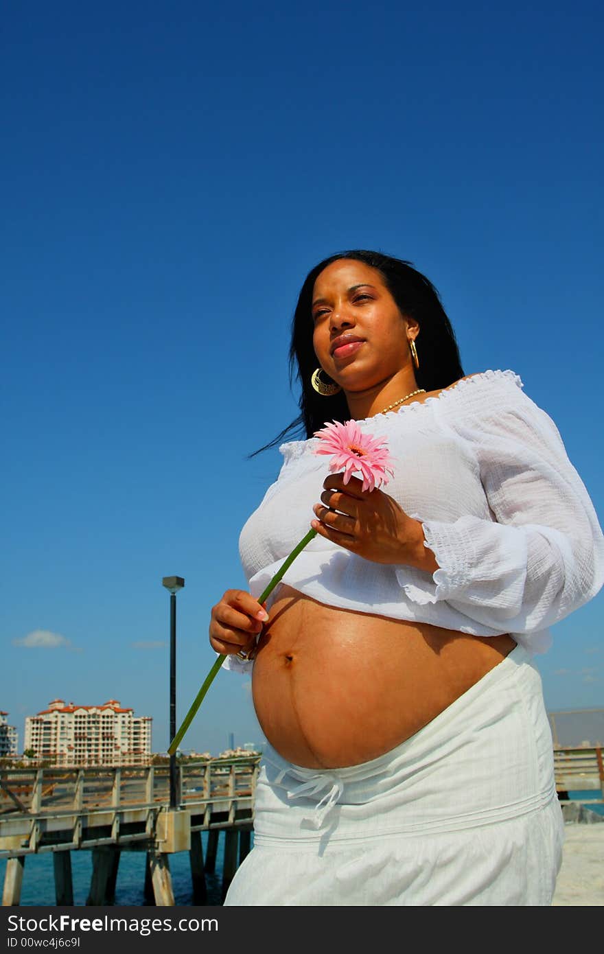 Pregnant woman with her stomach exposed and holding a pink flower.