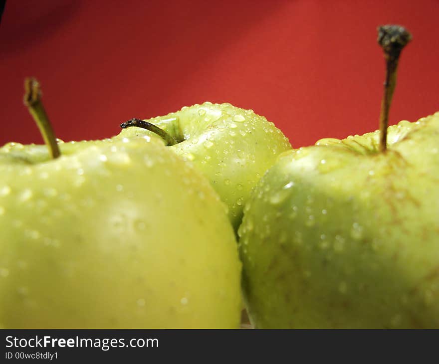 Fresh green apples closeup with water drops and red background. Fresh green apples closeup with water drops and red background