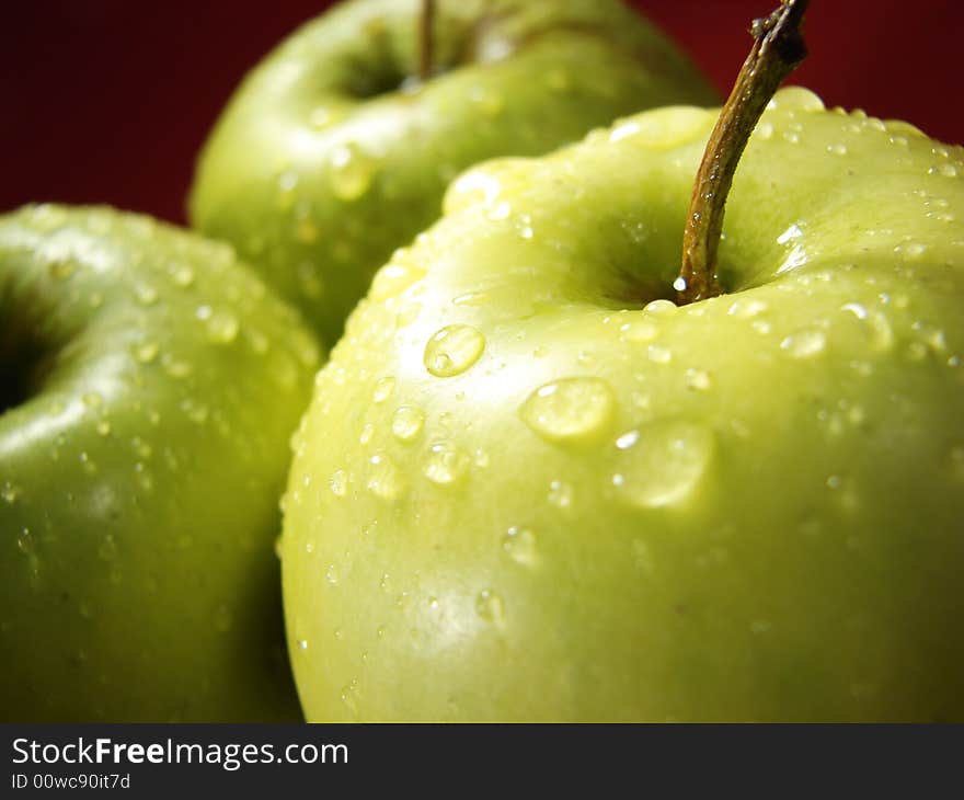 Fresh green apples closeup with water drops and red background. Fresh green apples closeup with water drops and red background