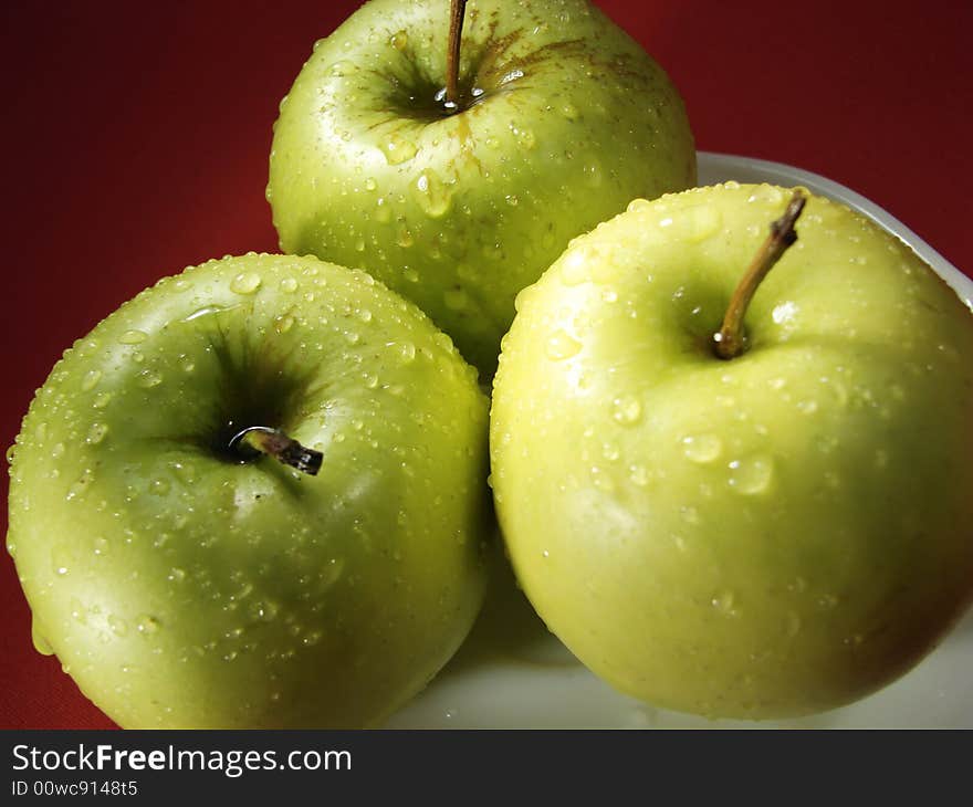 Fresh green apples closeup with water drops and red background. Fresh green apples closeup with water drops and red background