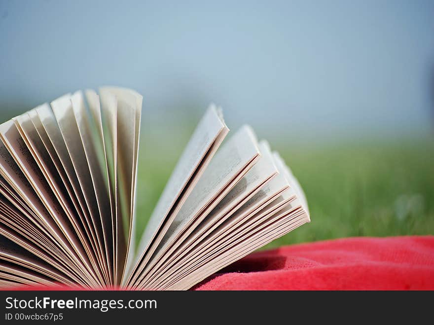 Shot of a book on a sunbathers towel with blurred meadow in background. Shot of a book on a sunbathers towel with blurred meadow in background