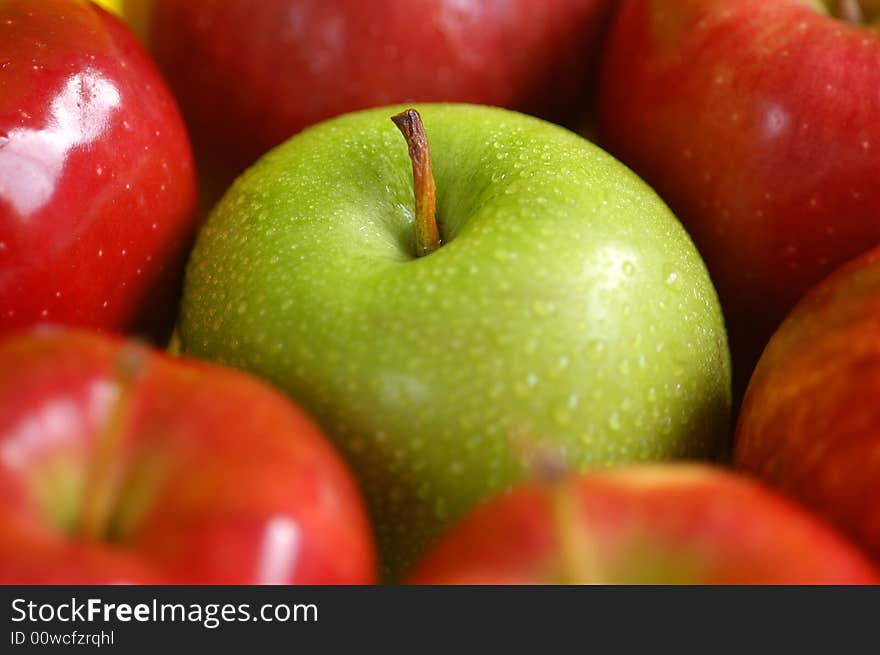 A green apple surrounded by red apples. A green apple surrounded by red apples.