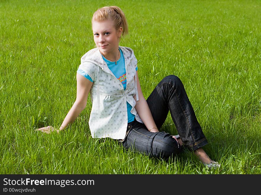 Young attractive girl sits on a green grass