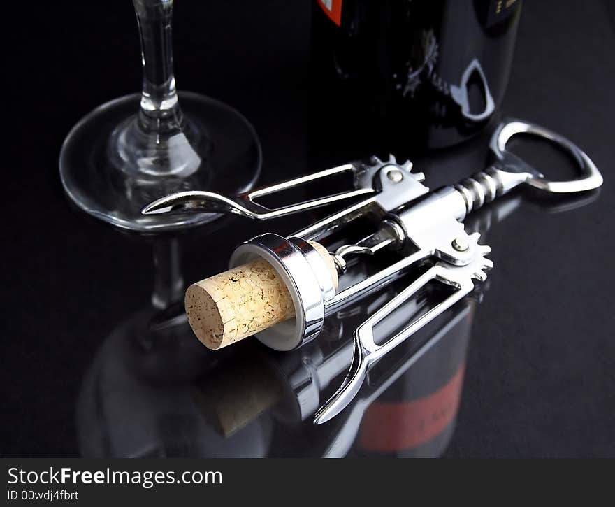 A corkscrew on a black table with cork, glass and bottle of wine. A corkscrew on a black table with cork, glass and bottle of wine.