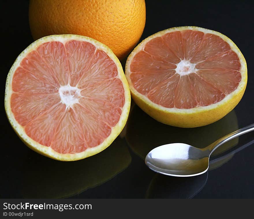 A pair of grapefruit, one sliced, with a spoon on a black table