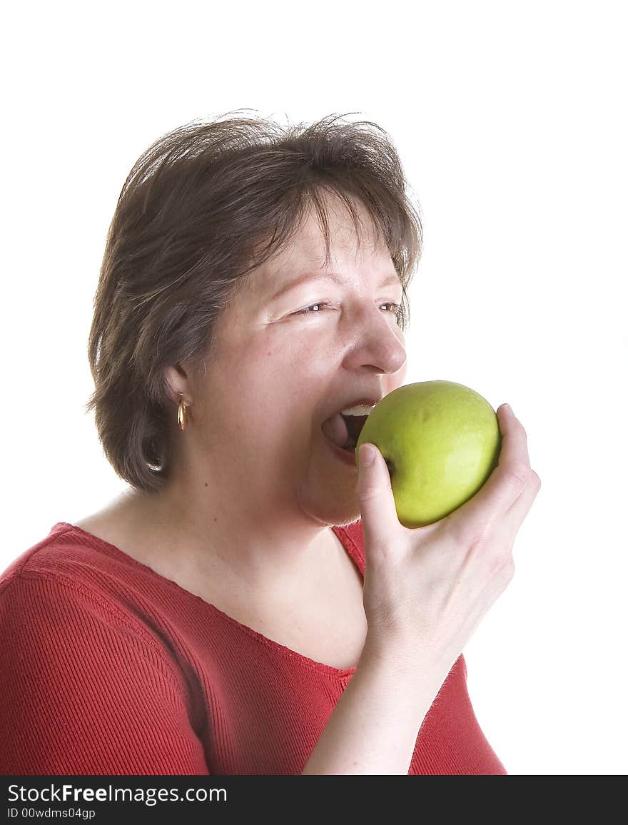 An attractive middle aged woman wearing a red blouse and eating a green apple. An attractive middle aged woman wearing a red blouse and eating a green apple