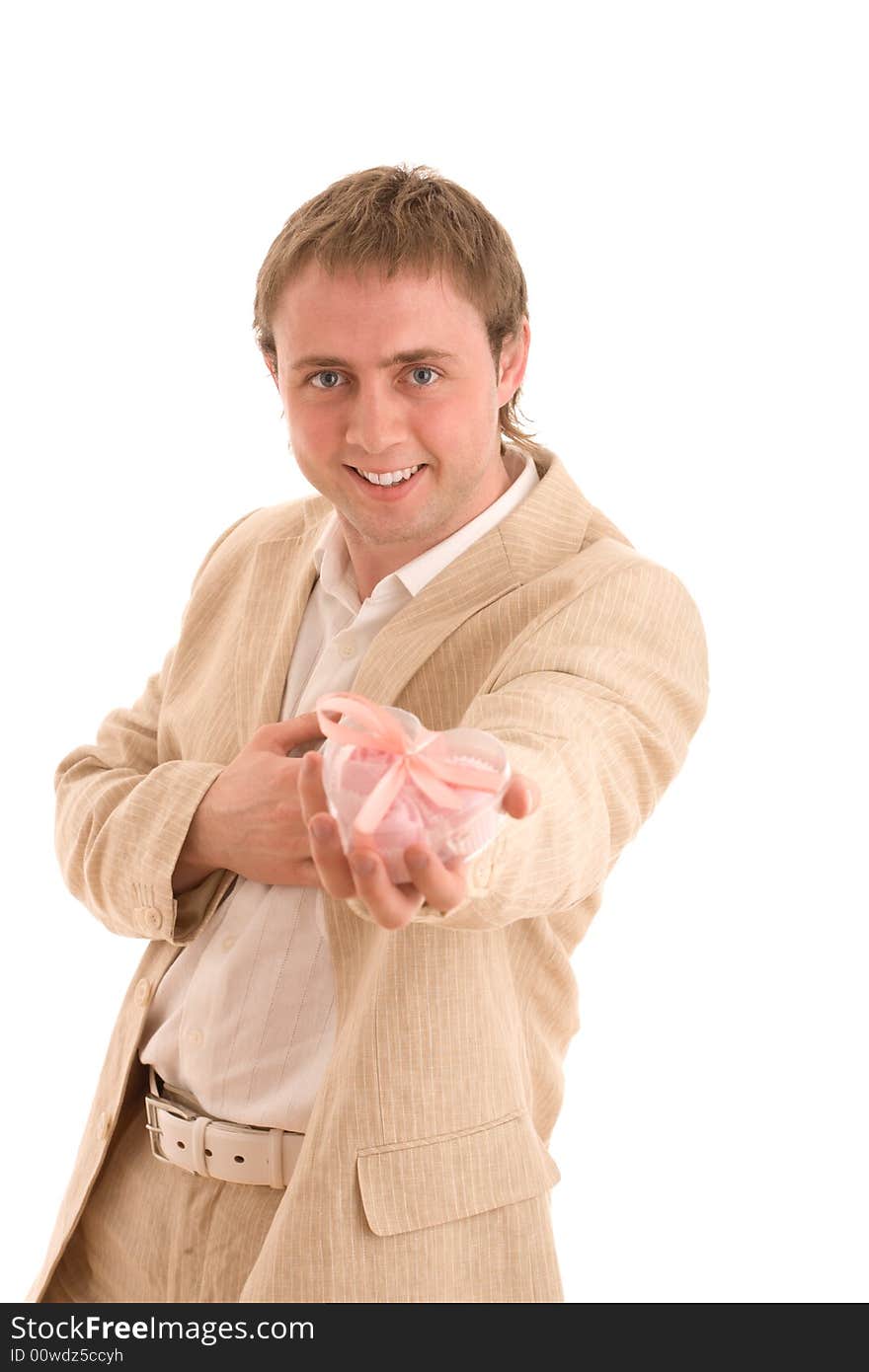 A smiling young man give a gift in a nice pink heart shaped box and place another hand at own heart. Isolated on white.