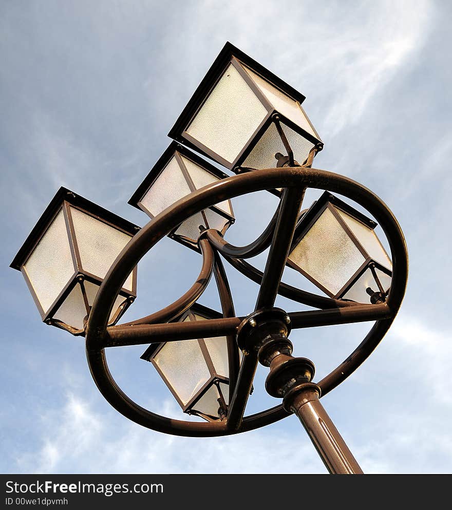 Three ornate street lamps on a lamp post against sky