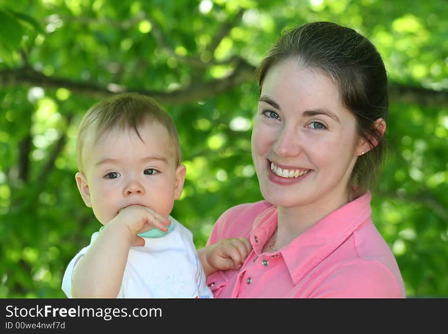 A beautiful young mother holding her baby with green foliage in the background. A beautiful young mother holding her baby with green foliage in the background.