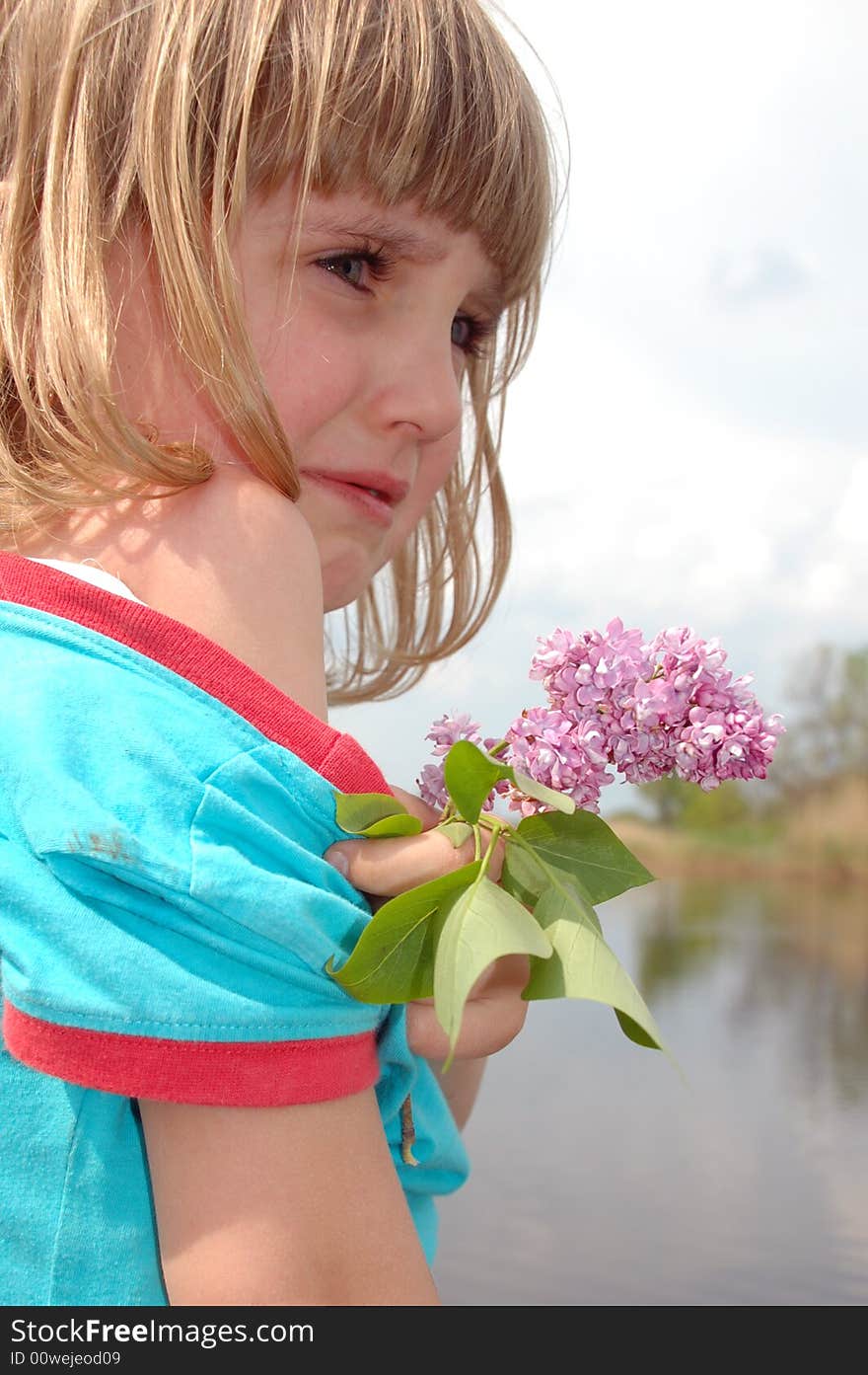 Little crying girl with lilac on the river bank