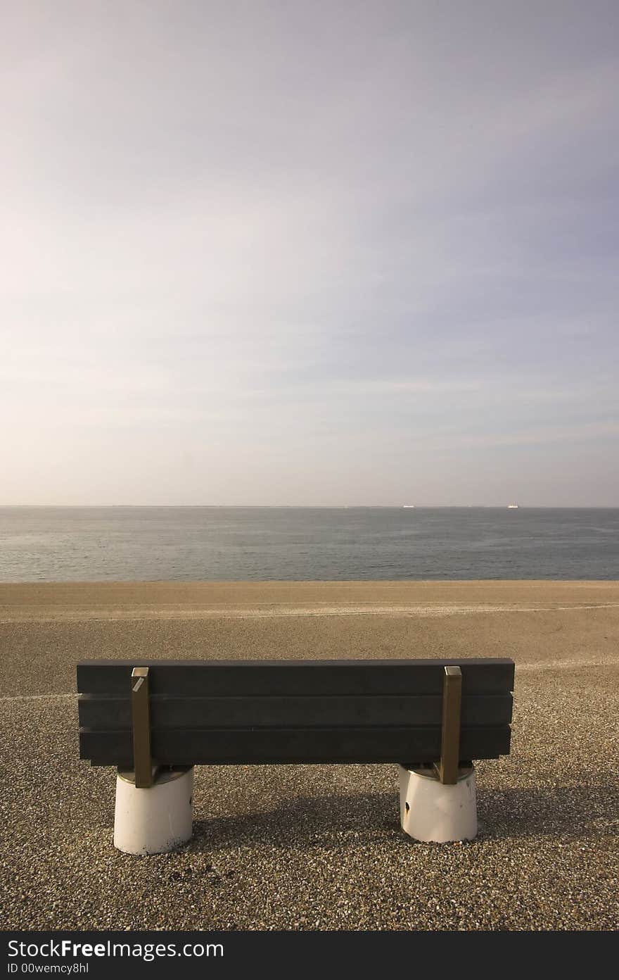 Wooden bench standing at the concrete covered seaside edge in Den Helder in Holland. Wooden bench standing at the concrete covered seaside edge in Den Helder in Holland