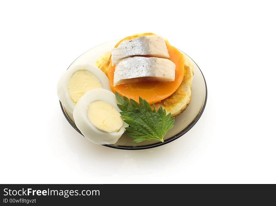 Pickled herring on a plate with boiled egg, carrot slices, pancake and nettle leaf, white background. Pickled herring on a plate with boiled egg, carrot slices, pancake and nettle leaf, white background