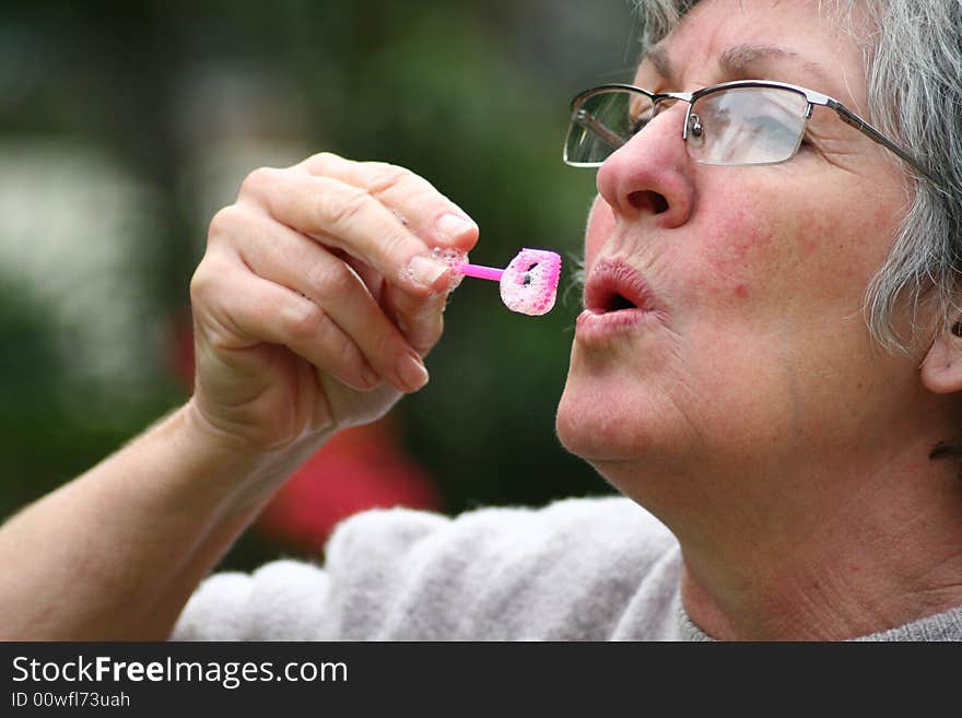 An old woman blowing bubbles like a child. An old woman blowing bubbles like a child