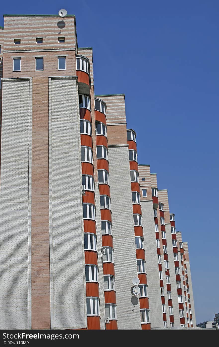 New brick multistoried building with red balconies on a background blue sky, social habitation