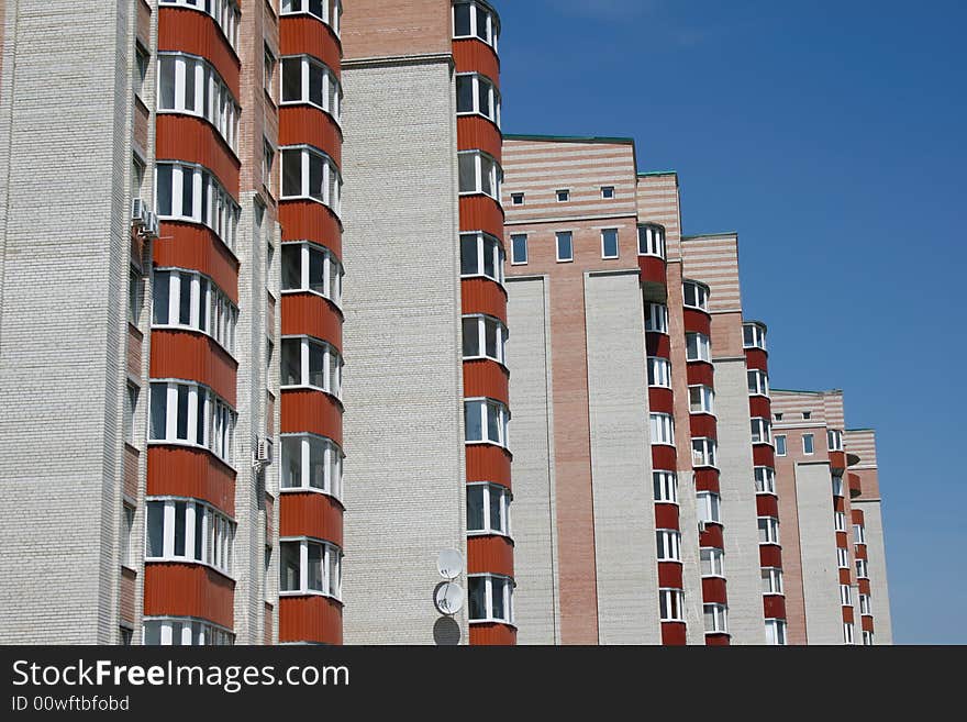 New brick multistoried building with red balconies on a background blue sky, social habitation