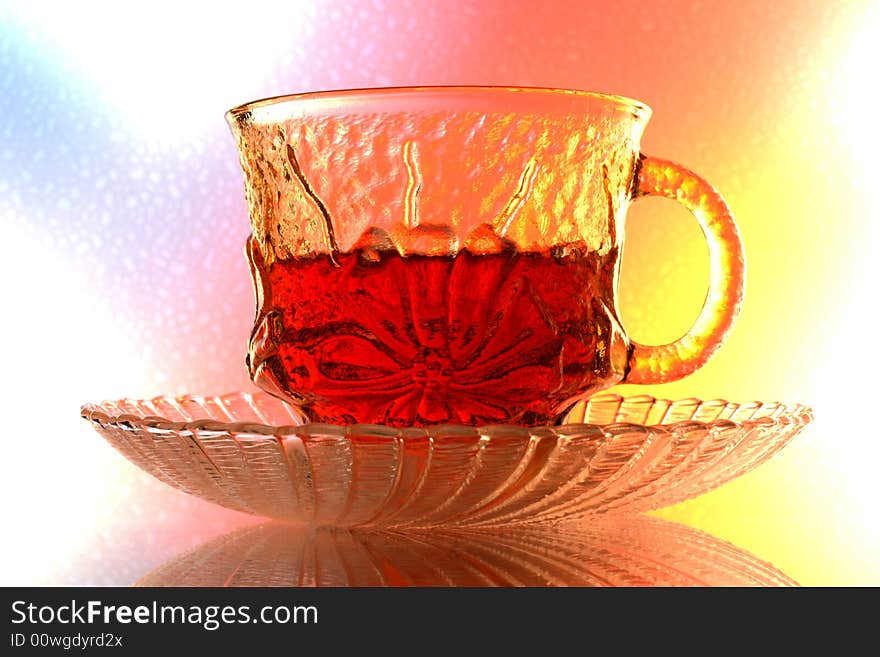 Close-up of glass teacup and saucer  against multi colored abstract background. Close-up of glass teacup and saucer  against multi colored abstract background