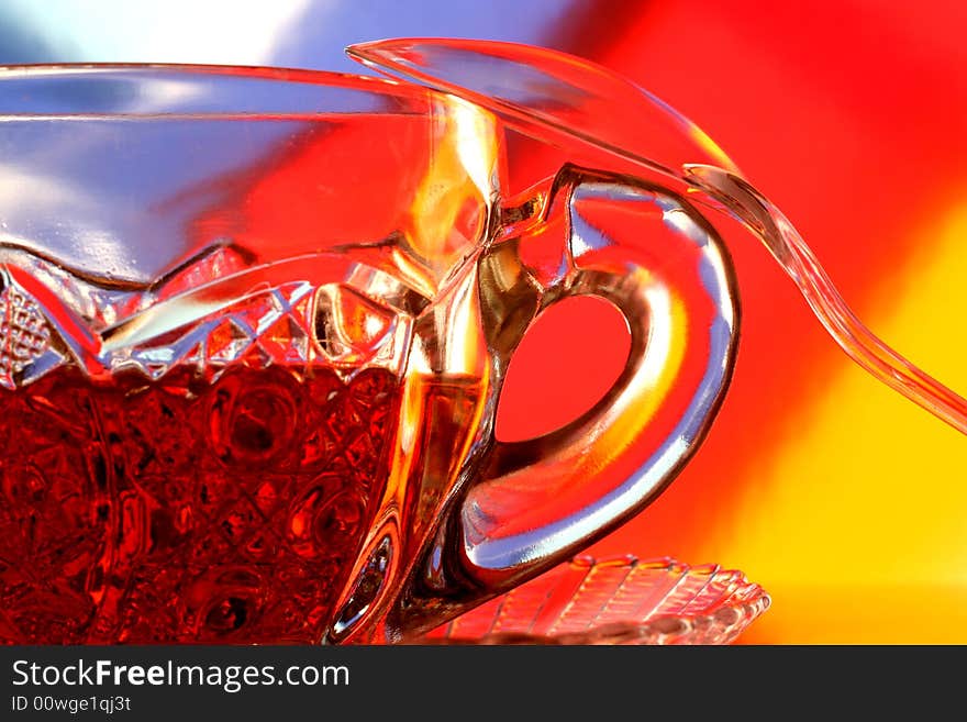 Close-up of glass teacup ,spoon and saucer against multi colored abstract background. Close-up of glass teacup ,spoon and saucer against multi colored abstract background