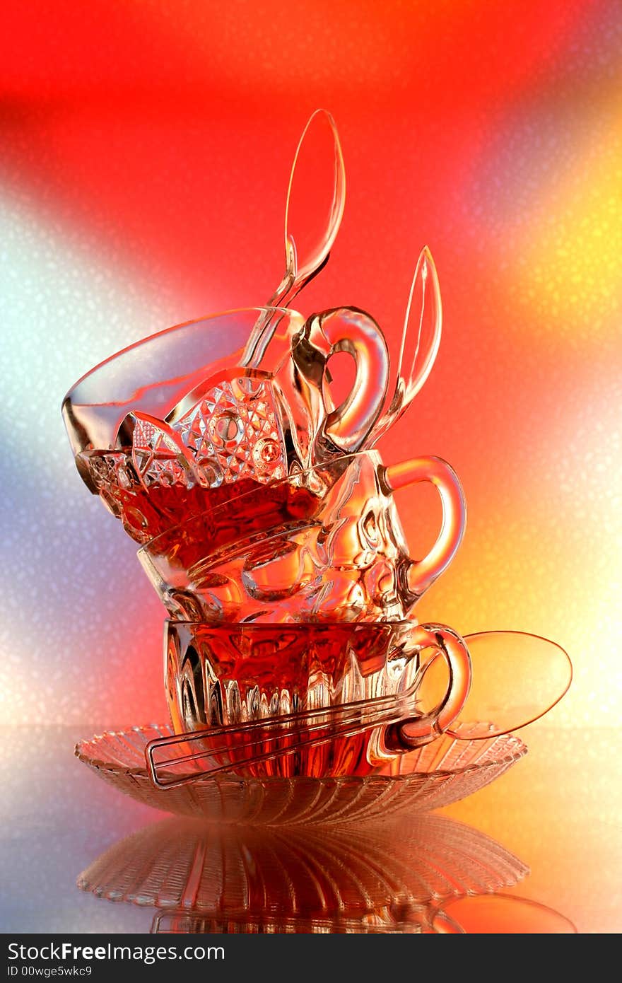 Close-up of glass teacup ,spoon and saucer  against multi colored abstract background. Close-up of glass teacup ,spoon and saucer  against multi colored abstract background