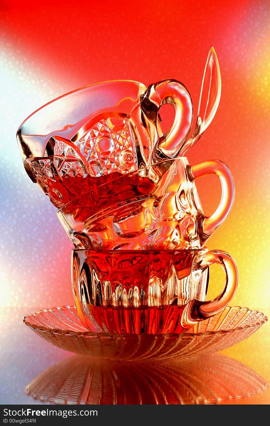 Close-up of glass teacup ,spoon and saucer against multi colored abstract background. Close-up of glass teacup ,spoon and saucer against multi colored abstract background