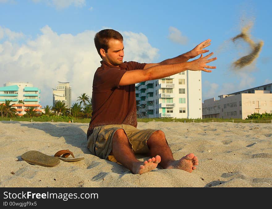 Man tossing sand to the side while sitting on the beach.