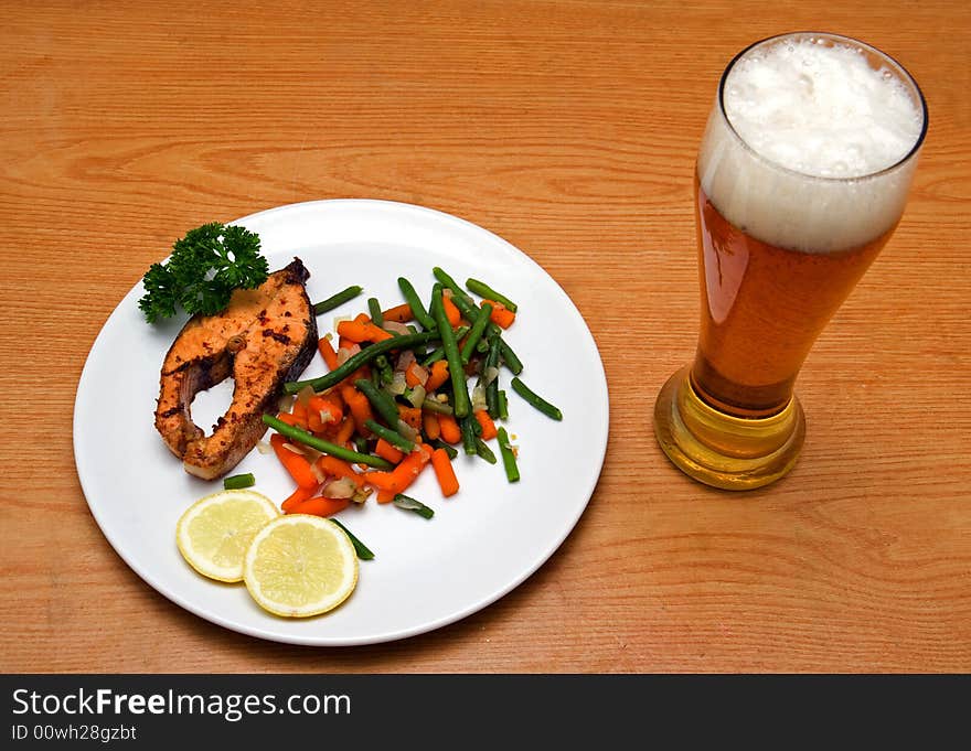 Light beer and fried salmon with vegetables on wooden background. Light beer and fried salmon with vegetables on wooden background