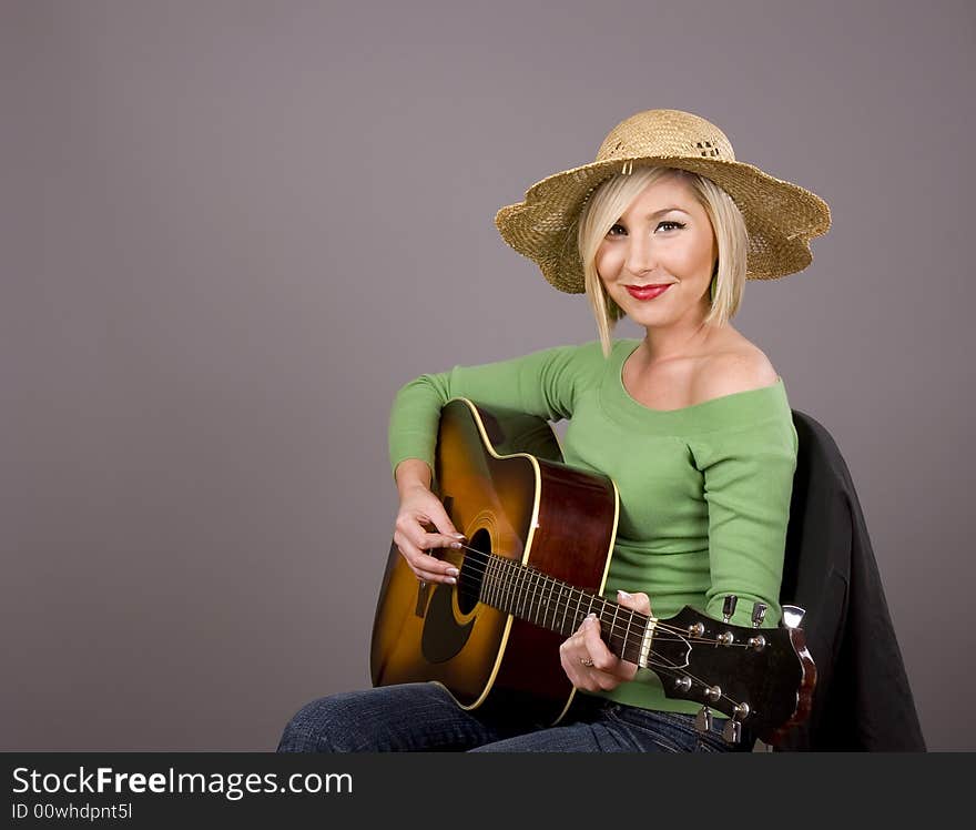 A blonde wearing a green blouse and a straw hat posing with a guitar. A blonde wearing a green blouse and a straw hat posing with a guitar