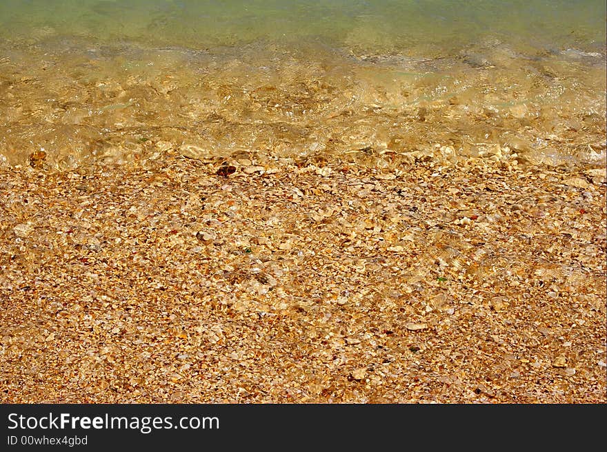 This is the picture of beach or coast . It is consist of the wet crushed sea shells and polished white , yellow , pink and red coloured fragments . We can see those trough wave waves reached beach and clear sea water in the upper parts of picture. This is the picture of beach or coast . It is consist of the wet crushed sea shells and polished white , yellow , pink and red coloured fragments . We can see those trough wave waves reached beach and clear sea water in the upper parts of picture.