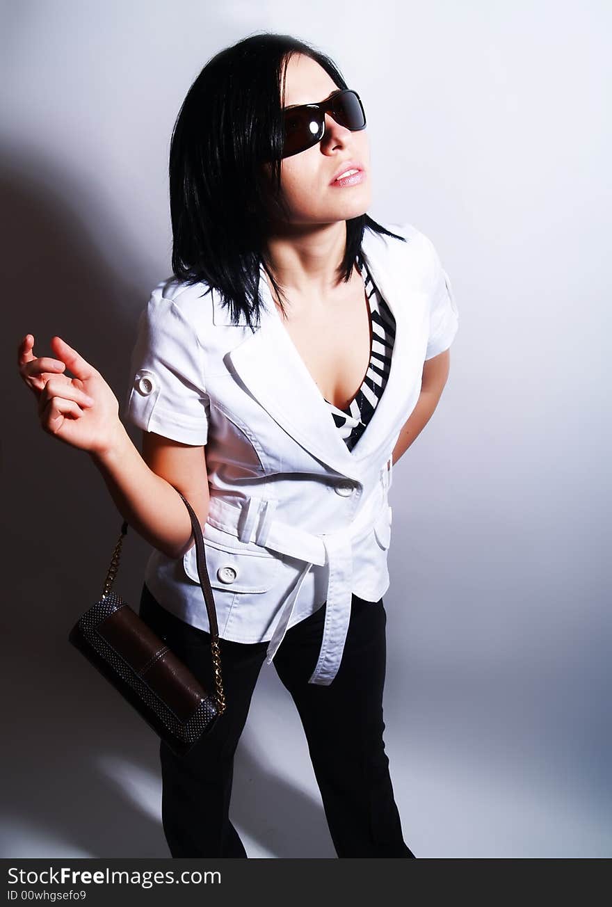 A high-key portrait about an attractive trendy lady with black hair who has a glamorous look. She is wearing sunglasses, black pants, a white coat and a stylish handbag. A high-key portrait about an attractive trendy lady with black hair who has a glamorous look. She is wearing sunglasses, black pants, a white coat and a stylish handbag.