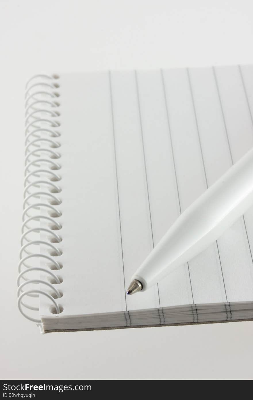 An open spiral bound notebook with lines paper and a white pen