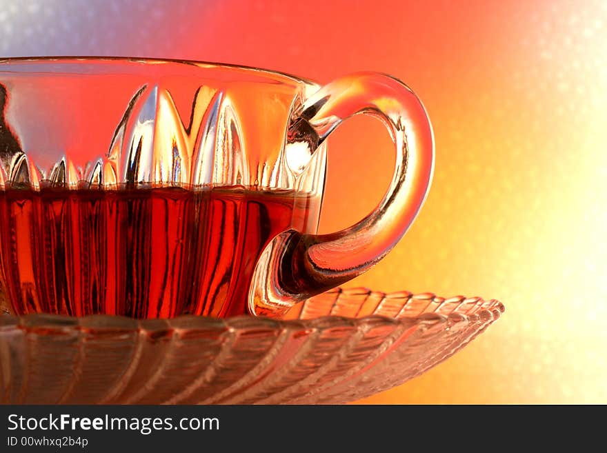 Close-up of glass teacup and saucer against multi colored abstract background. Close-up of glass teacup and saucer against multi colored abstract background