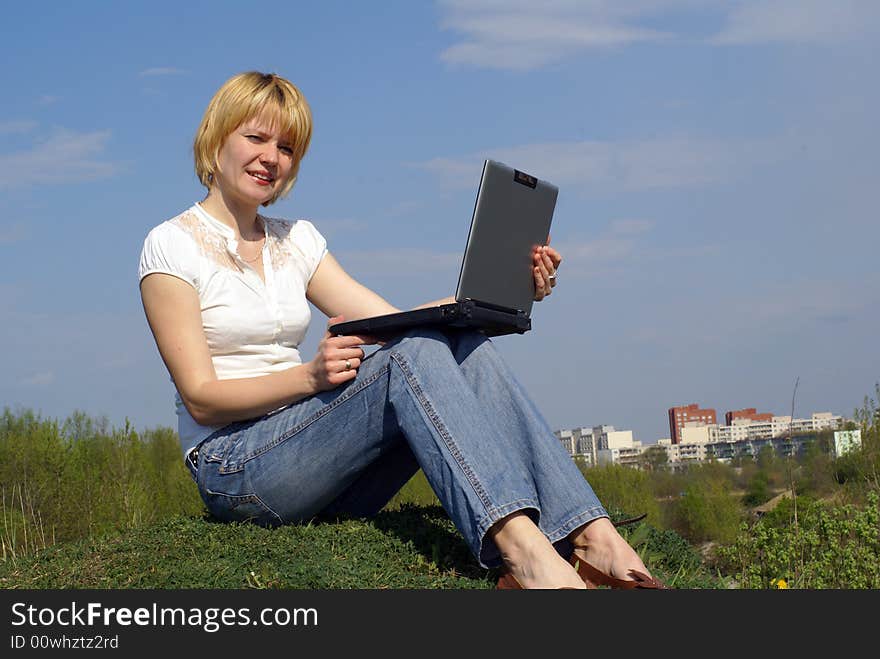 Woman is working with notebook on green grass and blue sky on background