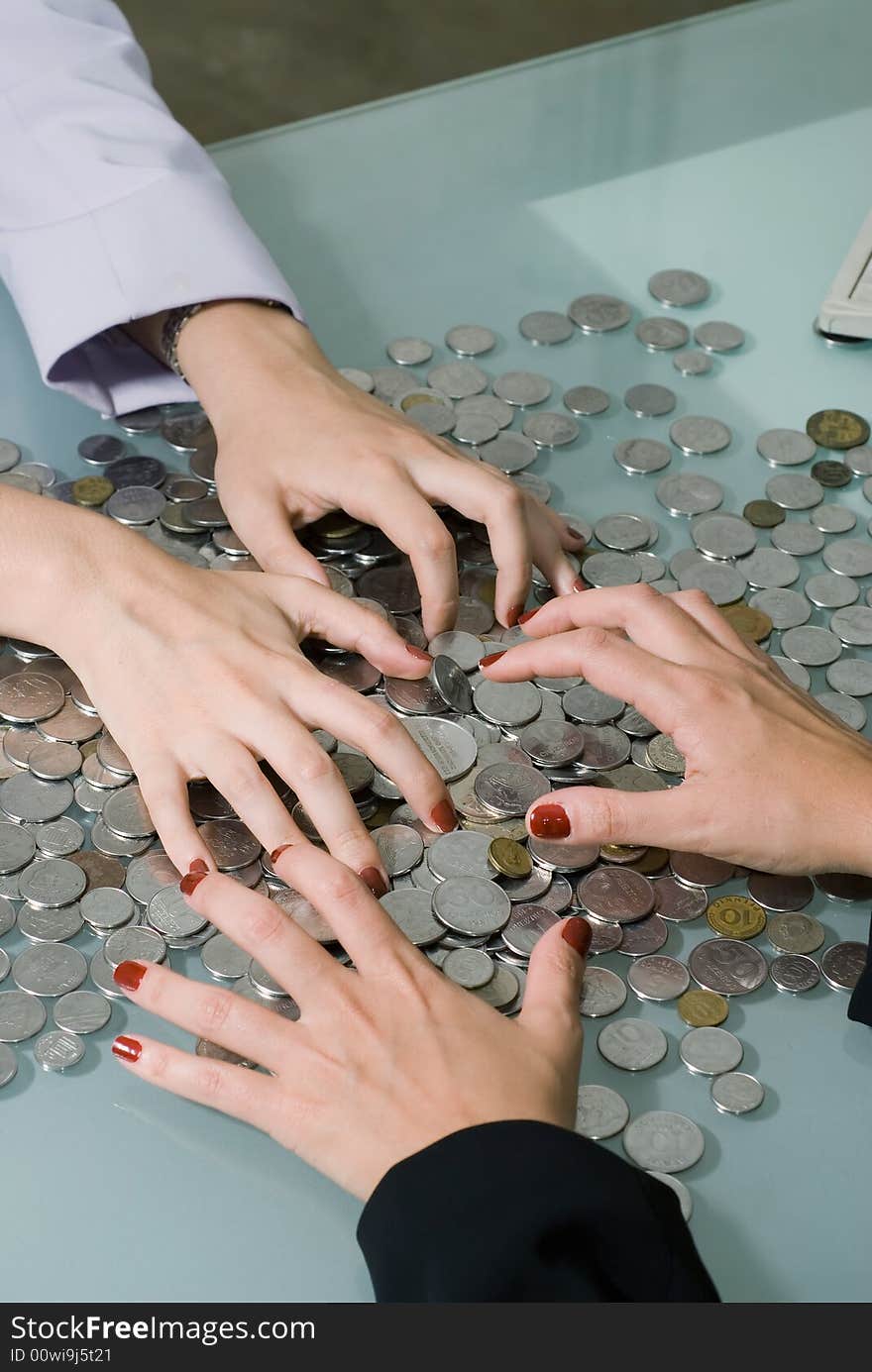 Close-up of two sets of female hands (on either side of a desk) grabbing at a large pile of coins in between them. Close-up of two sets of female hands (on either side of a desk) grabbing at a large pile of coins in between them.