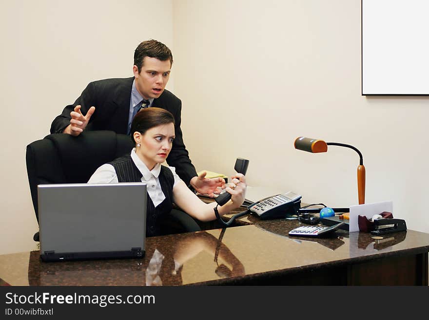 A shot of a businessman and businesswoman staring at a phone receiver.  The man is standing behind the woman, who's sitting at desk.  Both look confused. A shot of a businessman and businesswoman staring at a phone receiver.  The man is standing behind the woman, who's sitting at desk.  Both look confused.