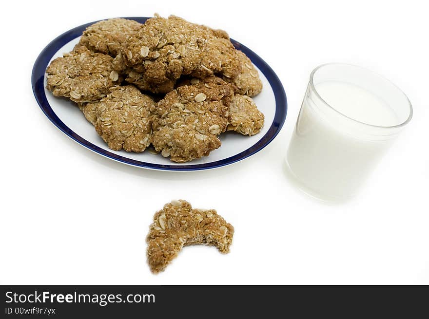 Plate of homemade oatmeal cookies and one cookie with a bite taken out of it and a glass of milk. Plate of homemade oatmeal cookies and one cookie with a bite taken out of it and a glass of milk