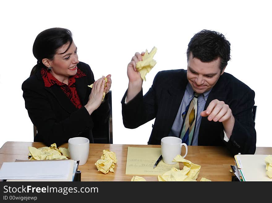 An isolated shot of businessman and businesswoman, in suits, sitting at a table topped with crumpled papers.  Both of the man and the woman look frustrated but happy. An isolated shot of businessman and businesswoman, in suits, sitting at a table topped with crumpled papers.  Both of the man and the woman look frustrated but happy.