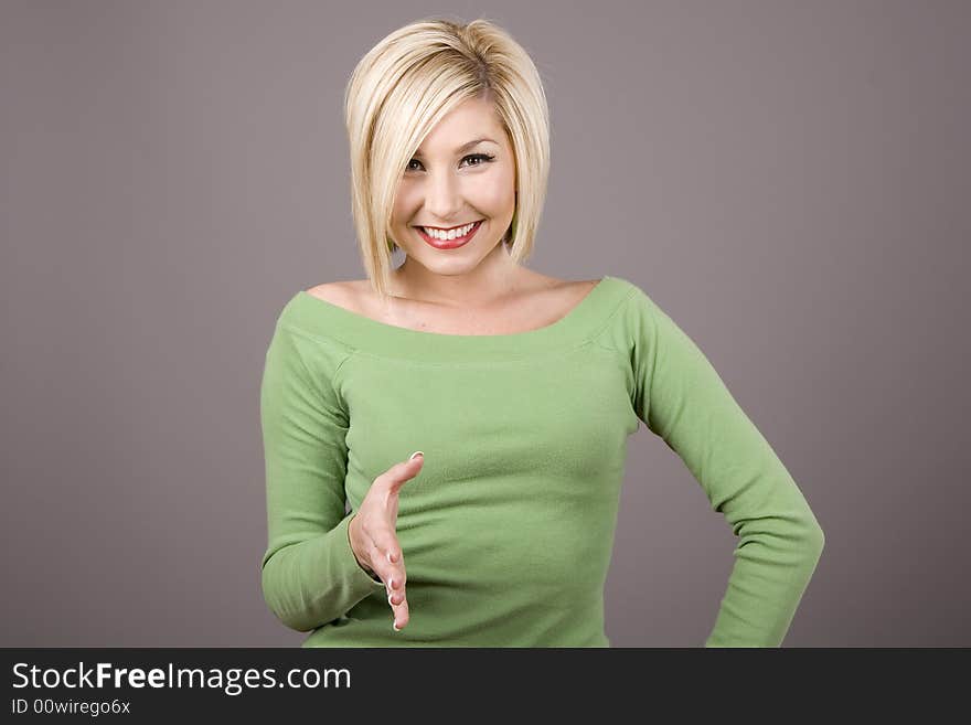 A blonde in a green blouse with her hand out for a shake. A blonde in a green blouse with her hand out for a shake