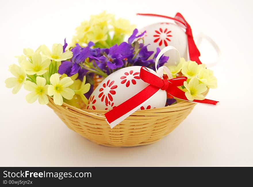 Easter eggs in basket with spring flowers on white background