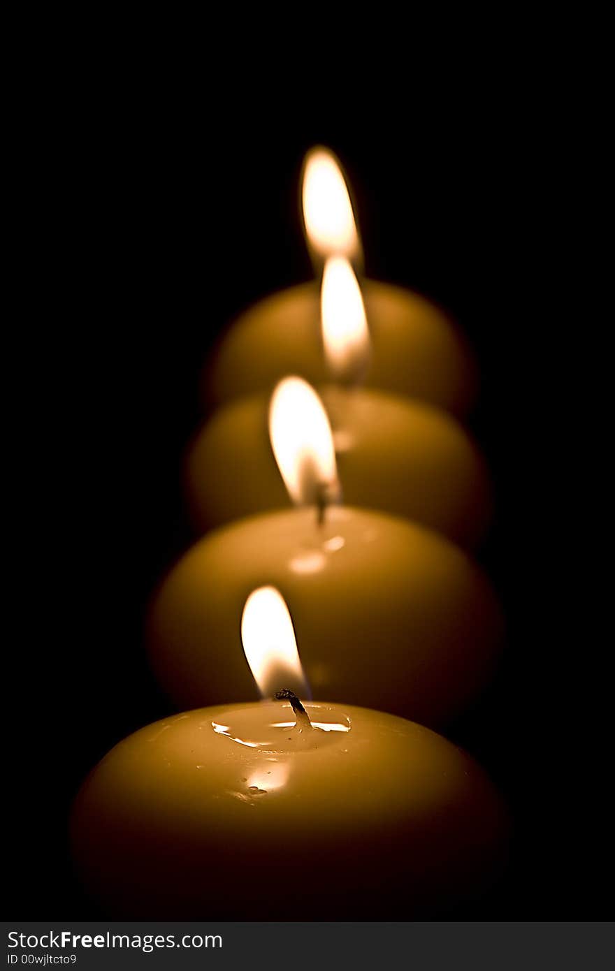 Four candles in a row on a black background.