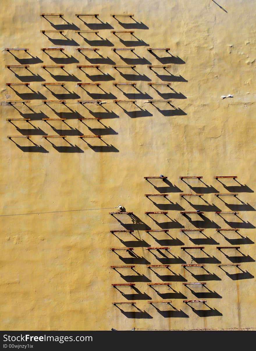 The wall of old house with strange iron construction which cast strict geometrical shadows. The wall of old house with strange iron construction which cast strict geometrical shadows.