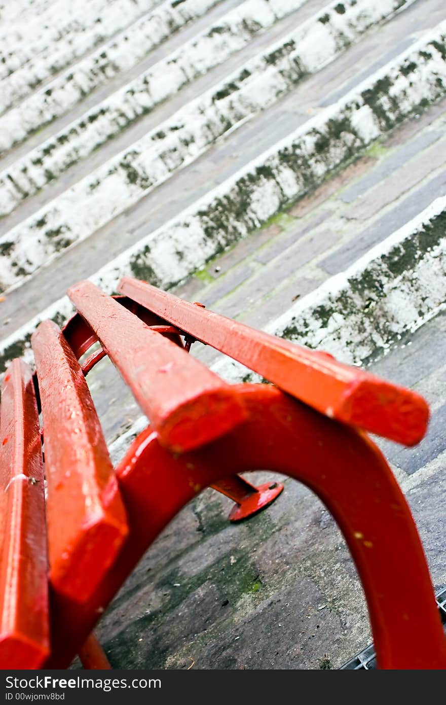 Close up of a red wooden seat with, on the back, old white stairs made of stones. This can be a concept image with the implication of a choice between stay and go. Useful also for relax and rest concept. Focus on the center of the seat. Close up of a red wooden seat with, on the back, old white stairs made of stones. This can be a concept image with the implication of a choice between stay and go. Useful also for relax and rest concept. Focus on the center of the seat.