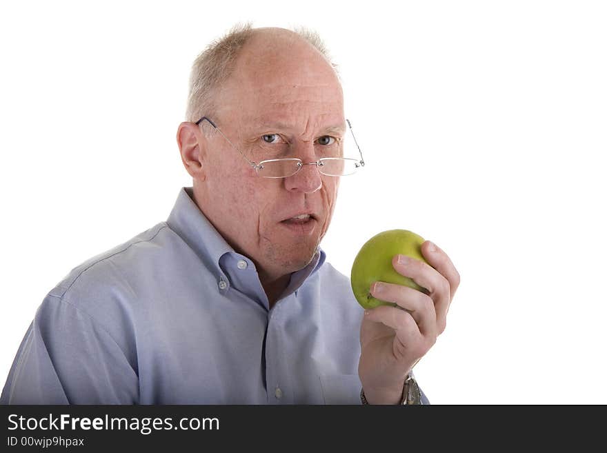 An older guy in a blue shirt and glasses holding an apple and looking at camera. An older guy in a blue shirt and glasses holding an apple and looking at camera