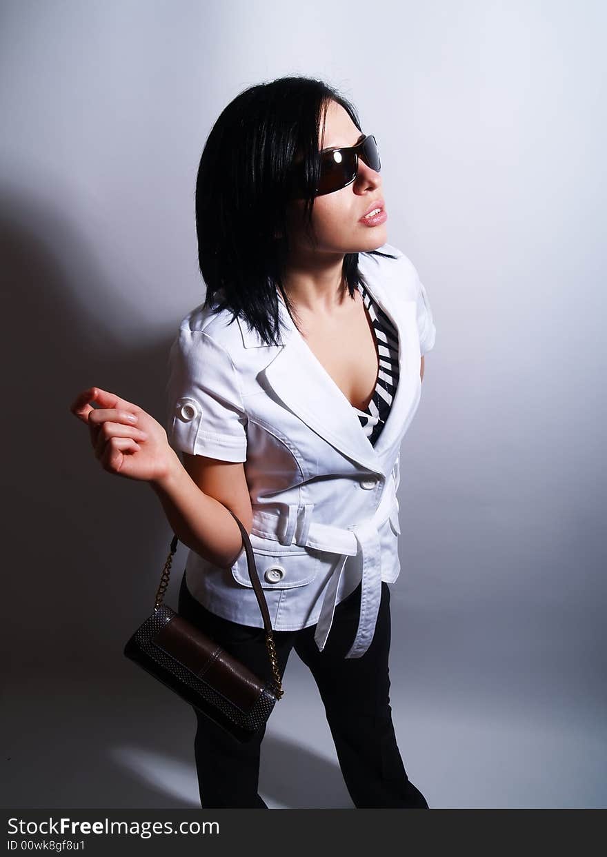 A high-key portrait about an attractive trendy lady with black hair who has a glamorous look. She is wearing sunglasses, black pants, a white coat and a stylish handbag. A high-key portrait about an attractive trendy lady with black hair who has a glamorous look. She is wearing sunglasses, black pants, a white coat and a stylish handbag.