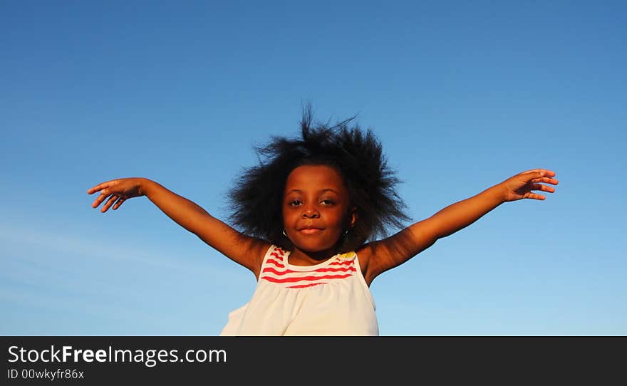 Young girl waving her arms with blue sky background. Young girl waving her arms with blue sky background.