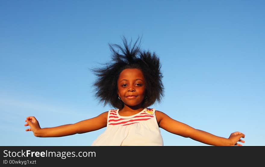 Young girl with her arms extended on blue sky background. Young girl with her arms extended on blue sky background.