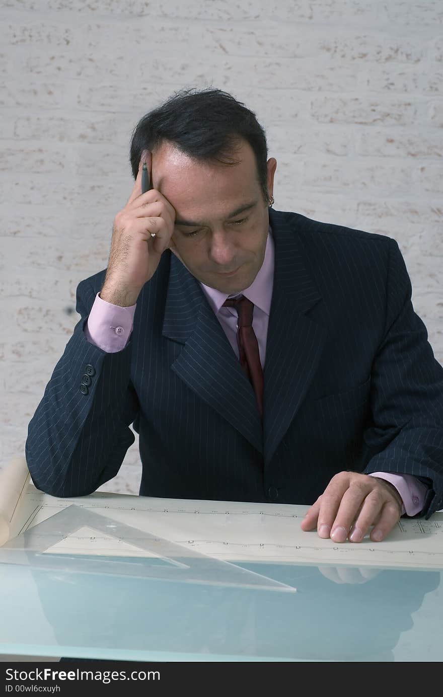 Latin american businessman reviewing plans and drawings on his office desk with his brow creased with concentration. Latin american businessman reviewing plans and drawings on his office desk with his brow creased with concentration