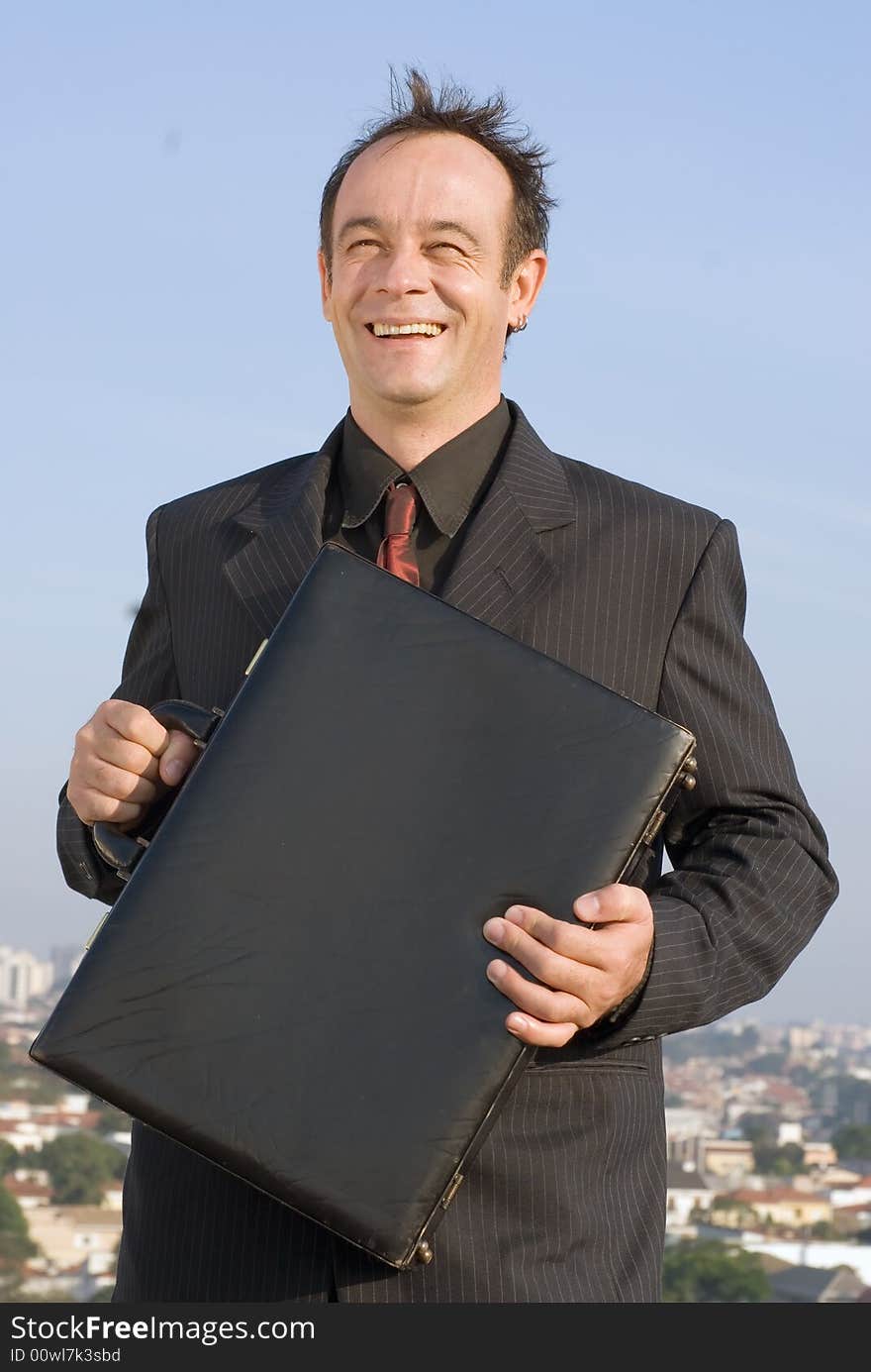 Businessman standing on a city rooftop and smiling while holding his briefcase close to his chest. Businessman standing on a city rooftop and smiling while holding his briefcase close to his chest