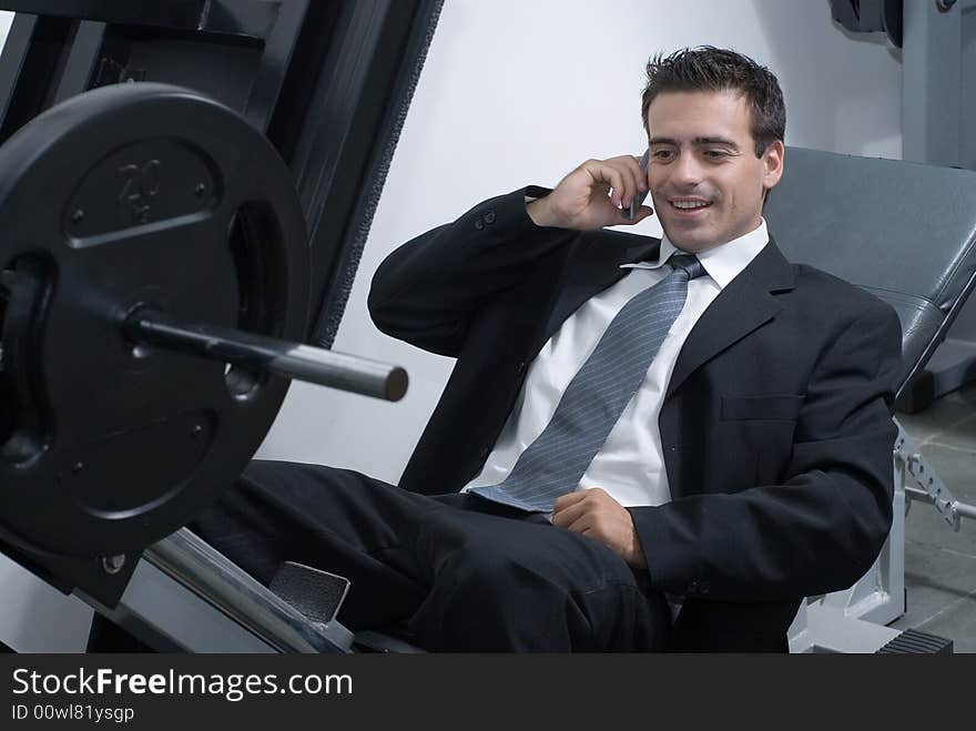 A shot of a businessman, in a suit, sitting on a weight machine talking on a cellphone. A shot of a businessman, in a suit, sitting on a weight machine talking on a cellphone.